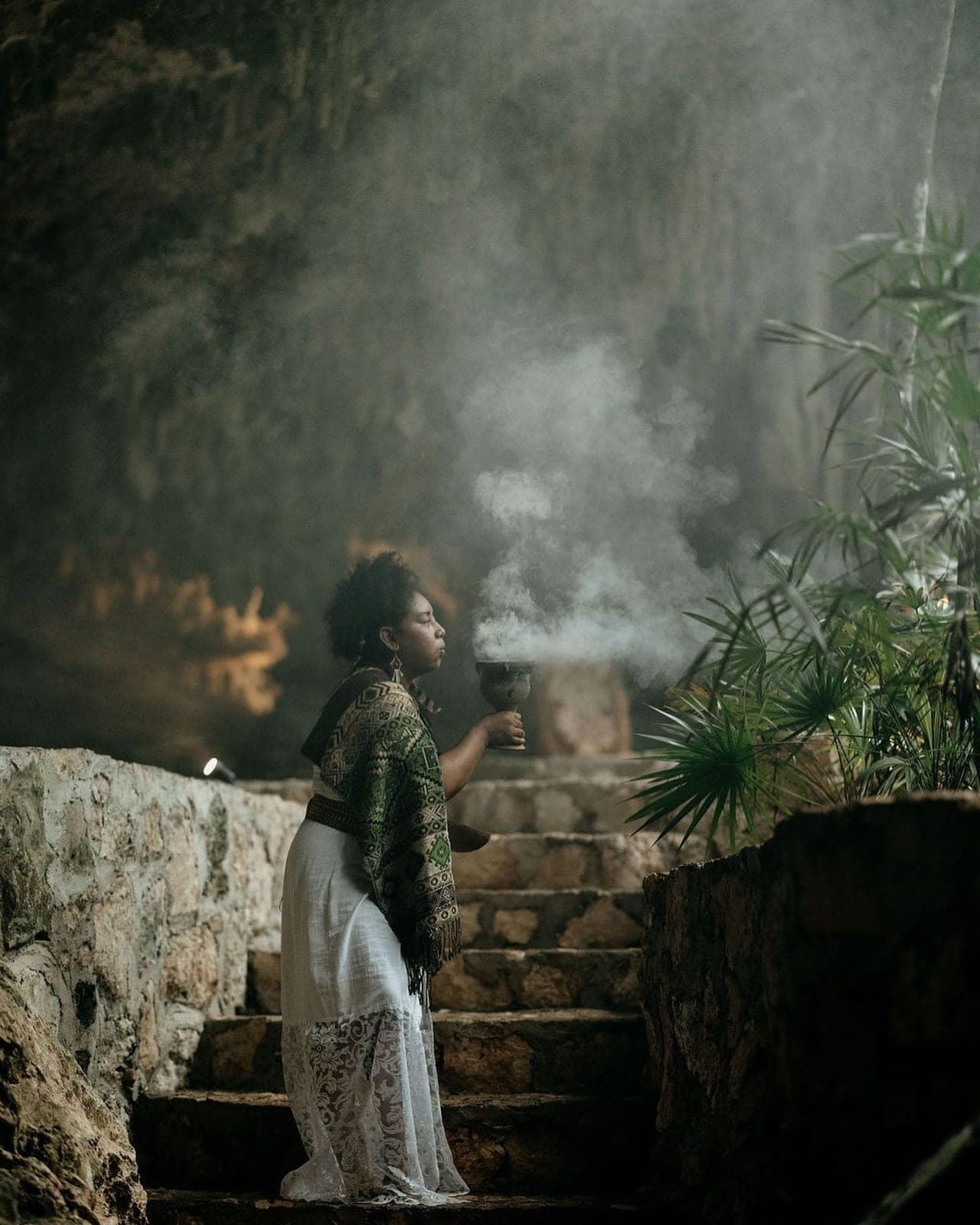 The ceremonial guide raising a smoking copal chalice on the stone steps inside the cave